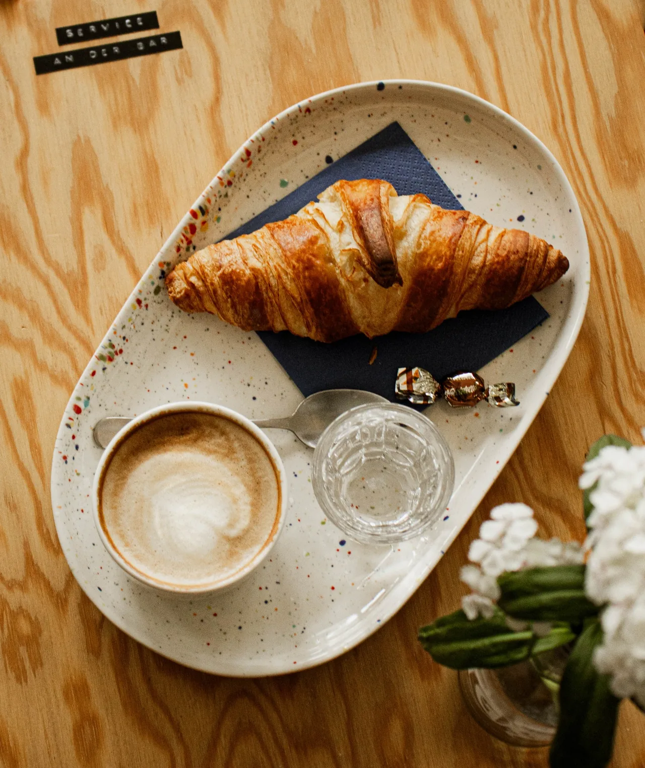 Kaffee und ein Gipfeli auf einem Holztisch mit einer kleinen Blume.