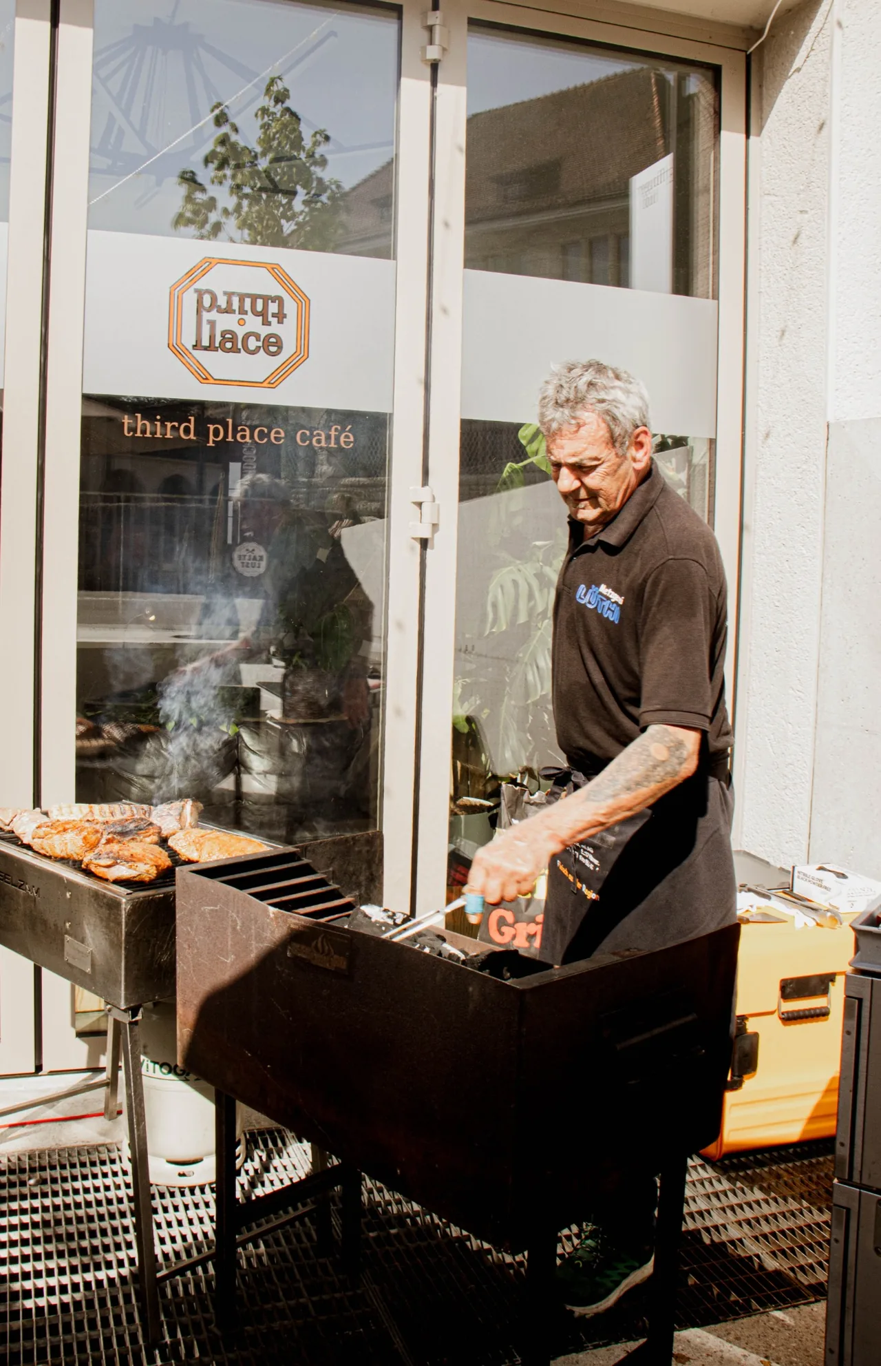 Grillen vor dem Third Place mit dem Logo im Fenster.